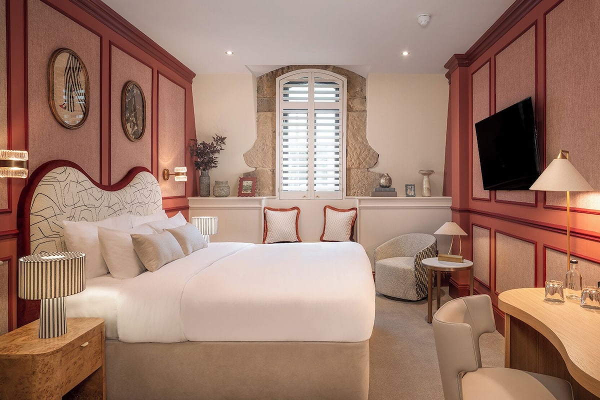 A bedroom with a large bed, bedside tables, a TV, and a window with blinds.