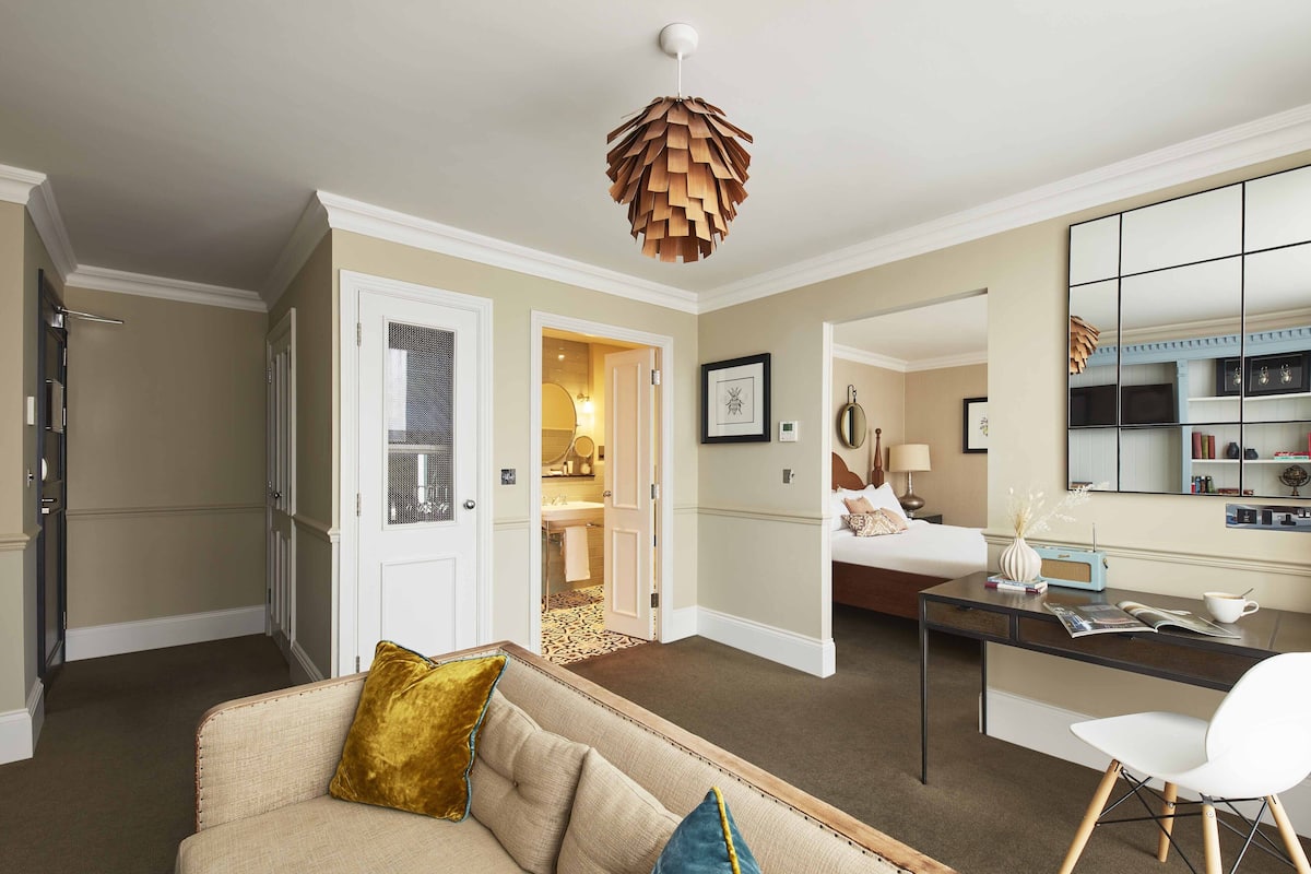 A hotel room with a sofa, a desk, a bed, a bathroom, and a dining area.