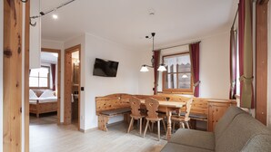 A cozy room with a wooden bench, a dining table with chairs, a sofa, and a TV mounted on the wall. - Chalet Tyrolian Apartments - by Familiaris - Pools 500 meters (Valdaora)
