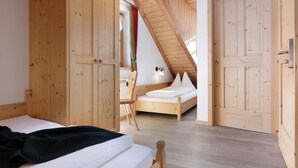 A bedroom with wooden walls, a sloped ceiling, and a bed with white bedding. - Chalet Tyrolian Apartments - by Familiaris - Pools 500 meters (Valdaora)