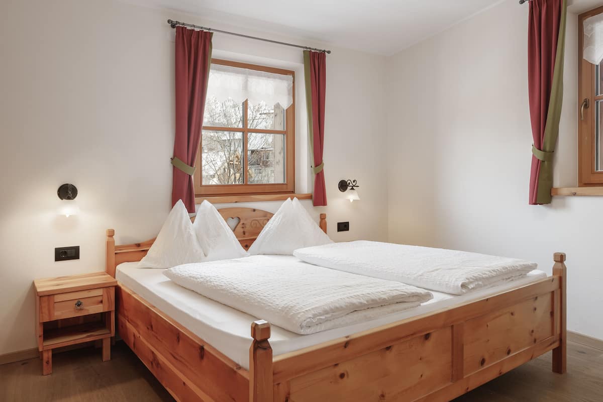 A wooden bed with white bedding, a nightstand, and a window with curtains.