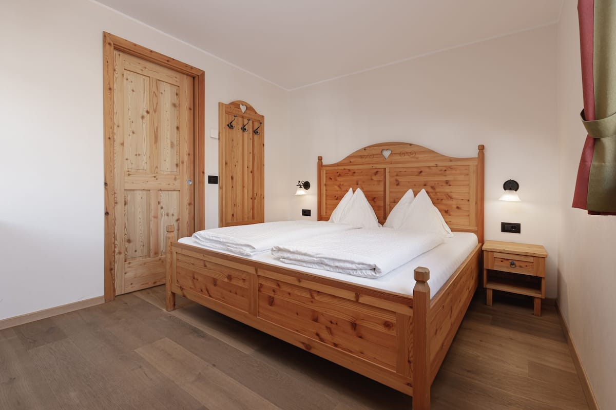A wooden bed with a headboard, a bedside table, and a wardrobe with a mirror.