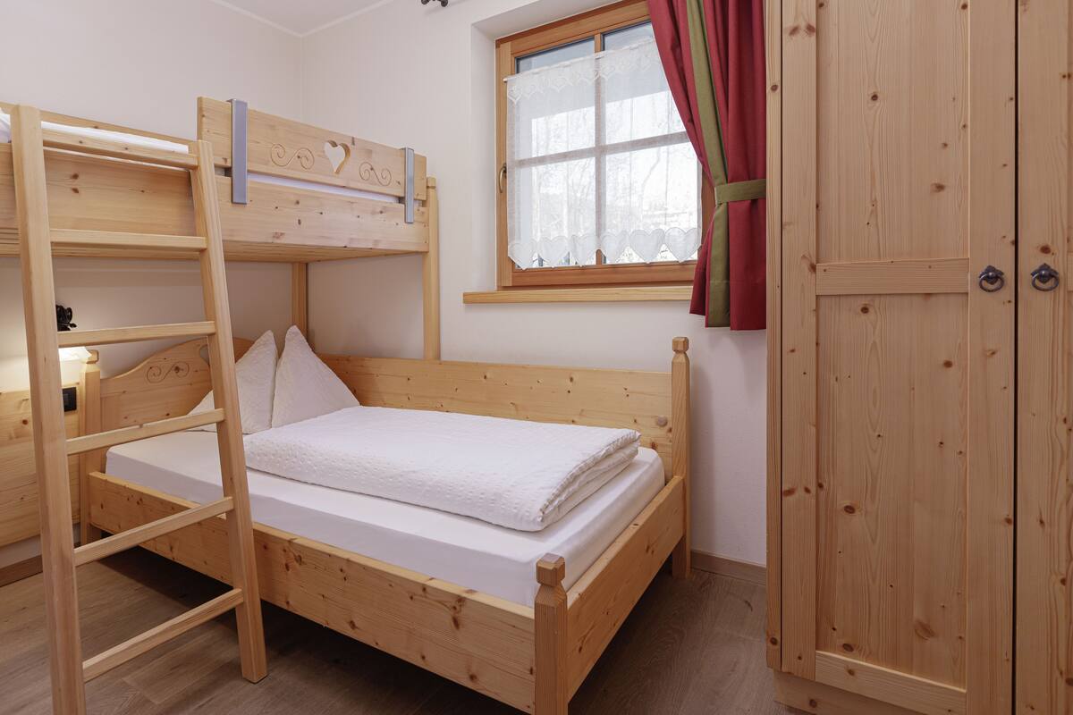 A bunk bed with a ladder, a window with curtains, and a wooden wardrobe.