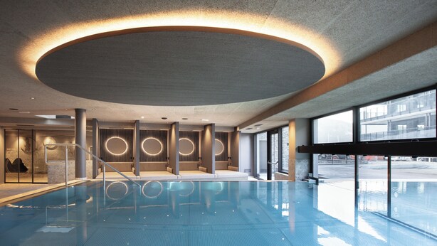 A modern indoor swimming pool with a circular ceiling design, large windows, and a clean, minimalist interior. - Chalet Tyrolian Apartments - by Familiaris - Pools 500 meters (Valdaora)