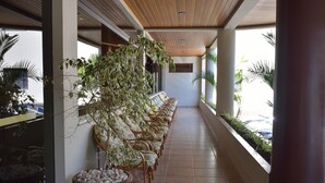Een overdekt terras met rieten stoelen en potplanten.