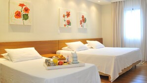 Een hotelkamer met twee bedden, witte lakens, een ontbijtplateau met fruit en een drankje, en bloemkunst aan de muur.