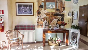 Una habitación acogedora con un mural antiguo, una silla de mimbre, una mesa de madera con una cesta y un farol blanco.
