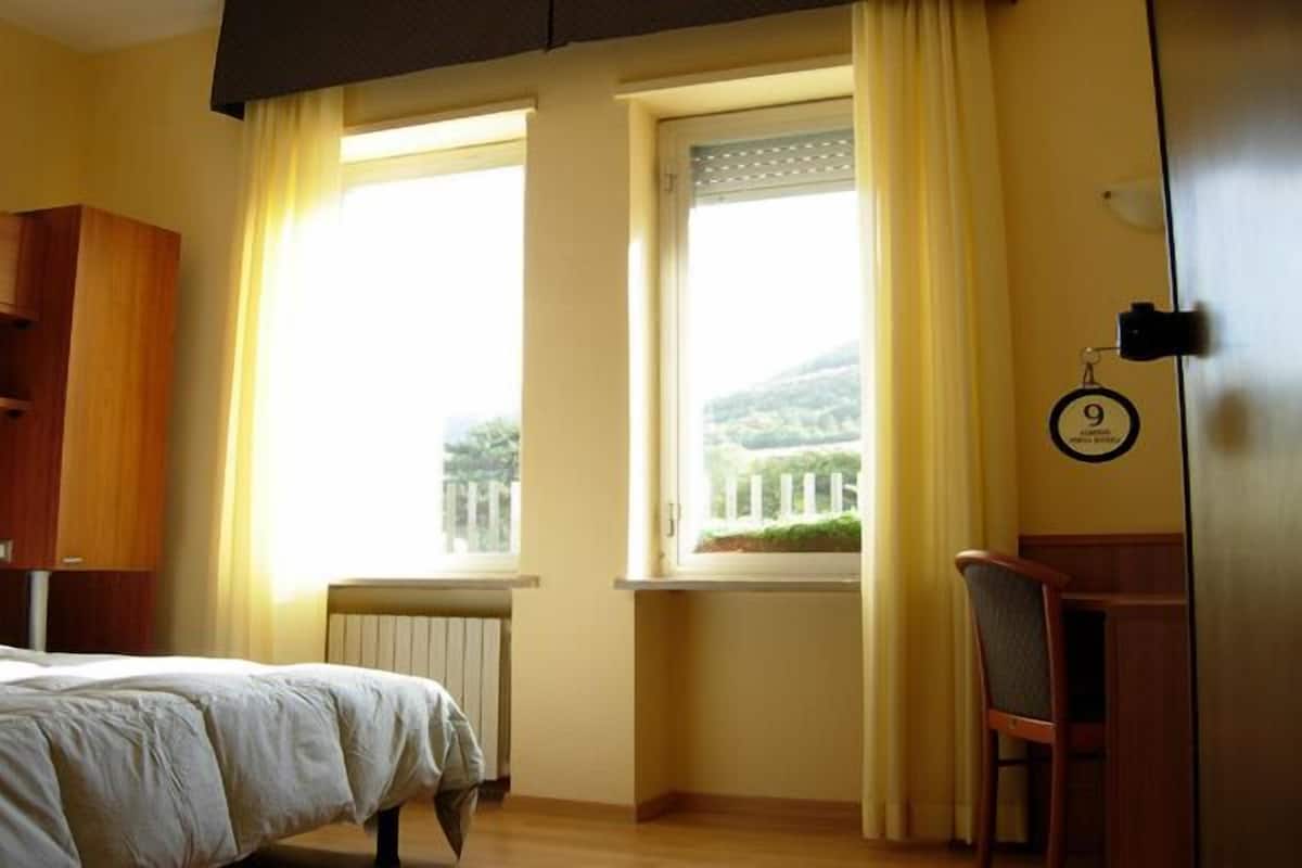 Une chambre d’hôtel avec un lit, une chaise, une fenêtre avec des rideaux et un radiateur.