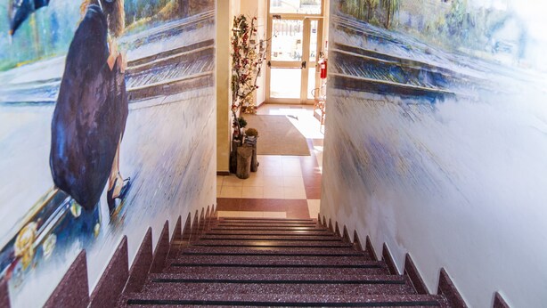 Una escalera con un mural en las paredes que muestra a una mujer con paraguas y un paisaje urbano.