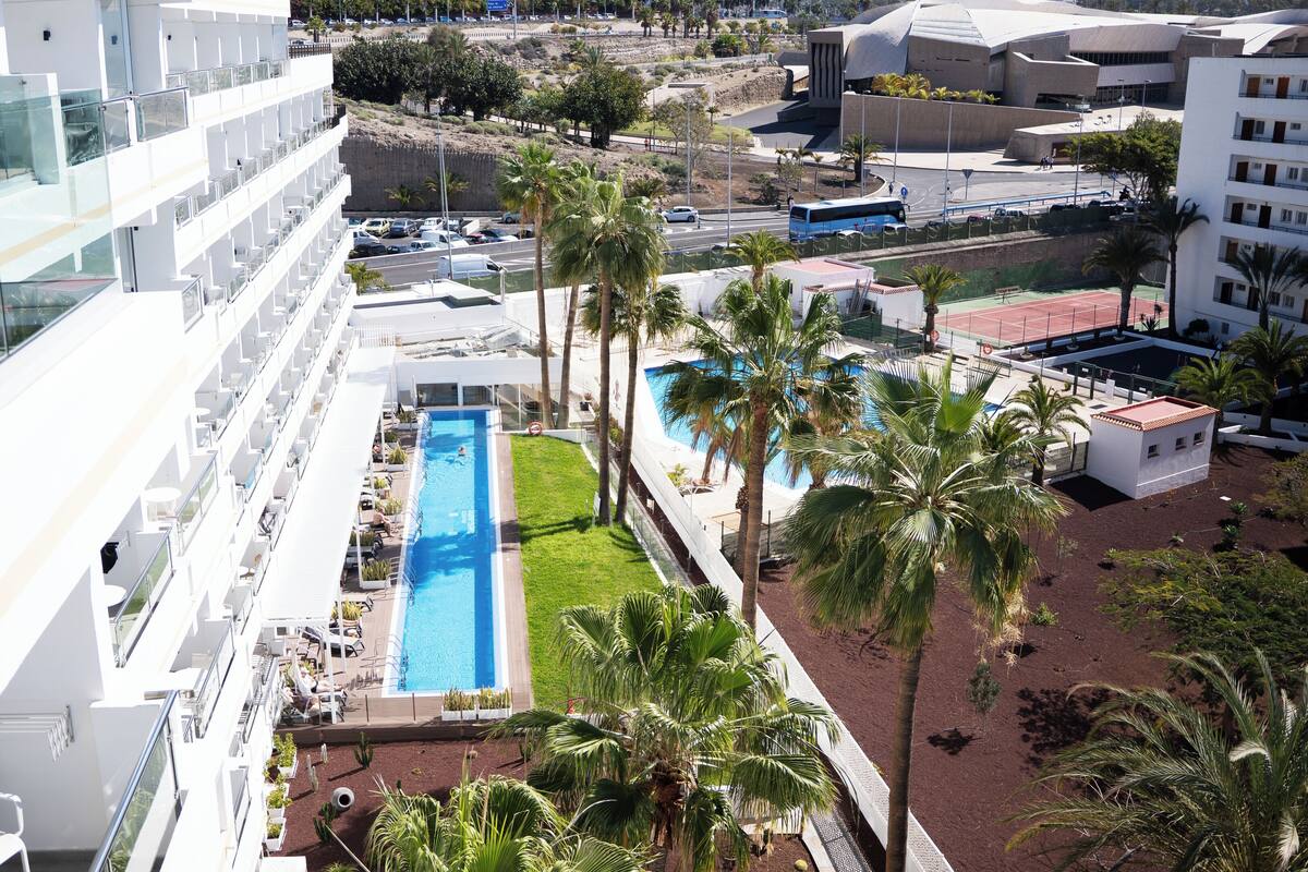 Un hôtel moderne doté d’une piscine sur le toit, de palmiers et offrant une vue sur la ville.