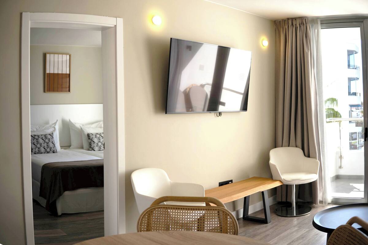 Une chambre d’hôtel avec un lit, un téléviseur fixé au mur, un bureau, deux chaises et une vue sur l’extérieur.