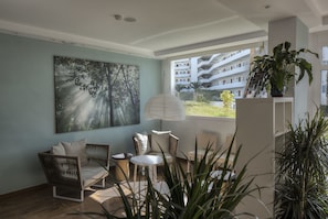 Relax in a stylish living space with a sofa, chairs, and a small table, surrounded by a large window offering a city view.