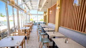 A restaurant with multiple tables and chairs, large windows, and a wooden wall panel.