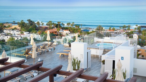 A rooftop pool area with sun loungers, umbrellas, and a view of the ocean.