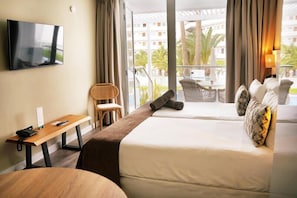 Quarto de hotel com duas camas, televisão, mesa de trabalho e varanda com vista para palmeiras e edifícios.