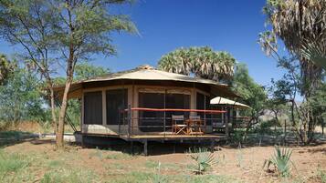 A safari lodge with a covered veranda, outdoor seating, and a dirt ground.