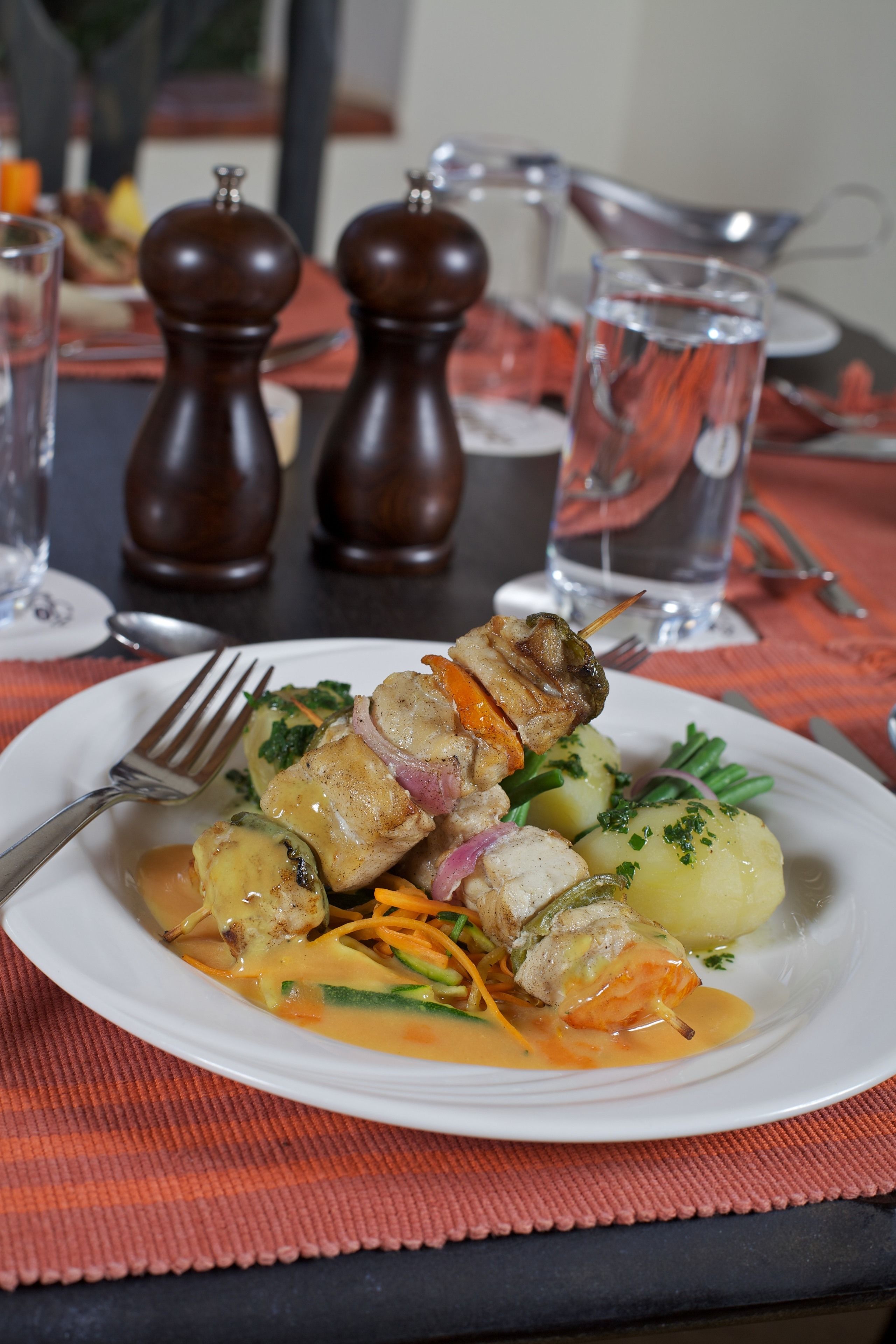 A plate of food with a fork and a glass of water on a table with a placemat.
