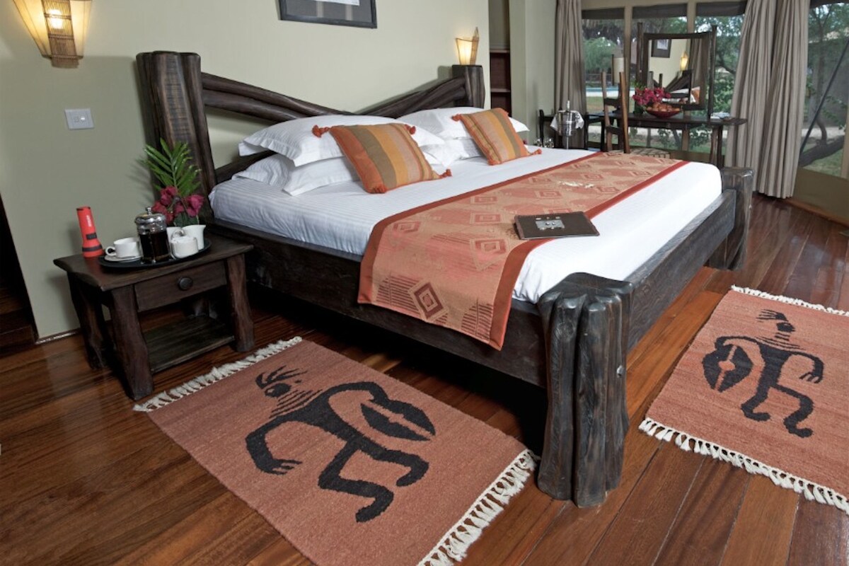 A spacious bedroom with a large bed, a nightstand, a bedside table, and a window with curtains.