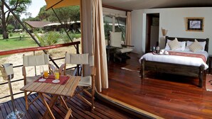 A wooden deck with a table and chairs, a bed with pillows, and a framed picture on the wall. - Ashnil Samburu Camp (Samburu)