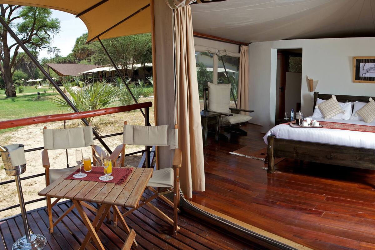 A wooden deck with a table and chairs, a bed with pillows, and a framed picture on the wall.