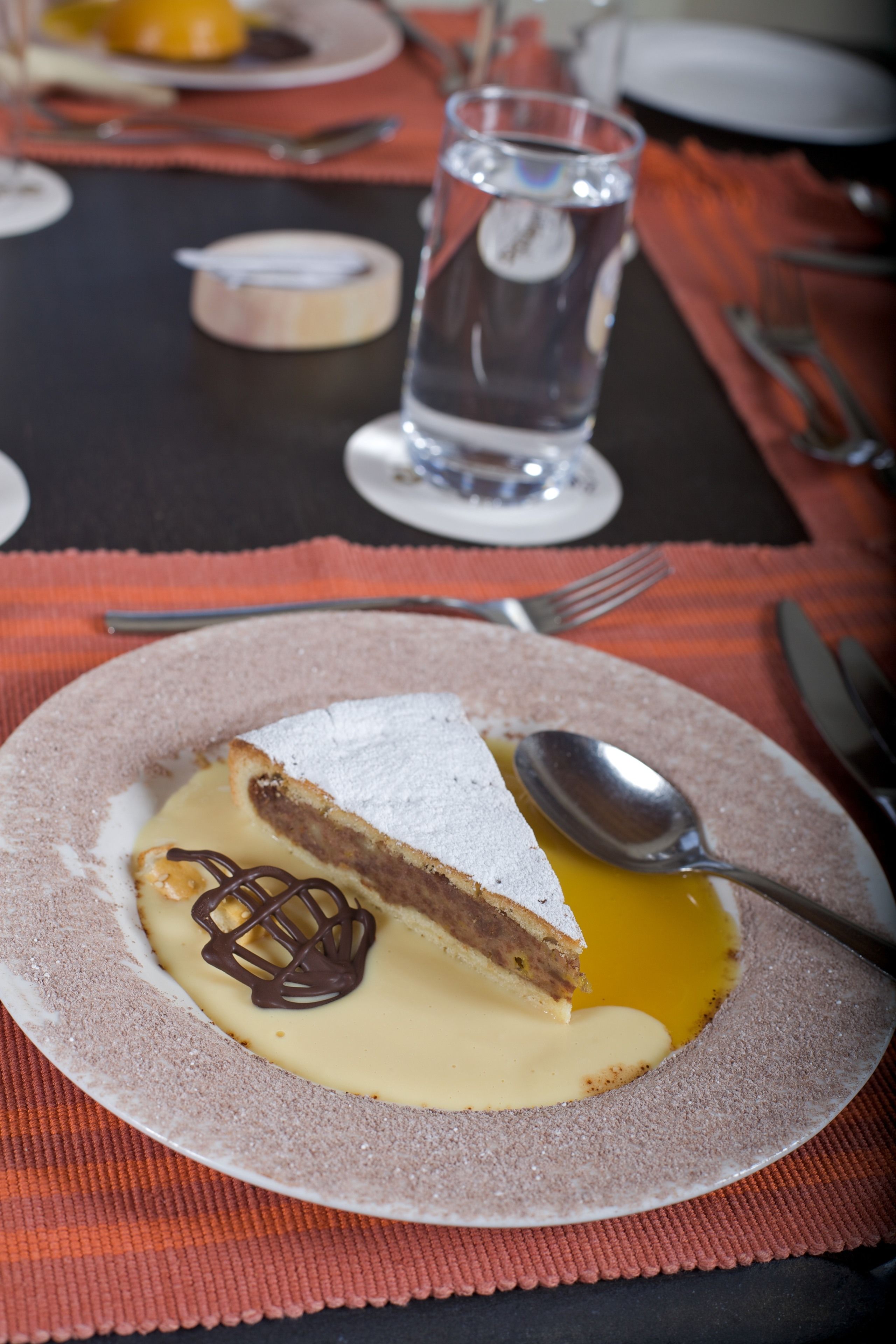 A dessert plate with a slice of cake, a spoon, and a glass of water on a table with a placemat.