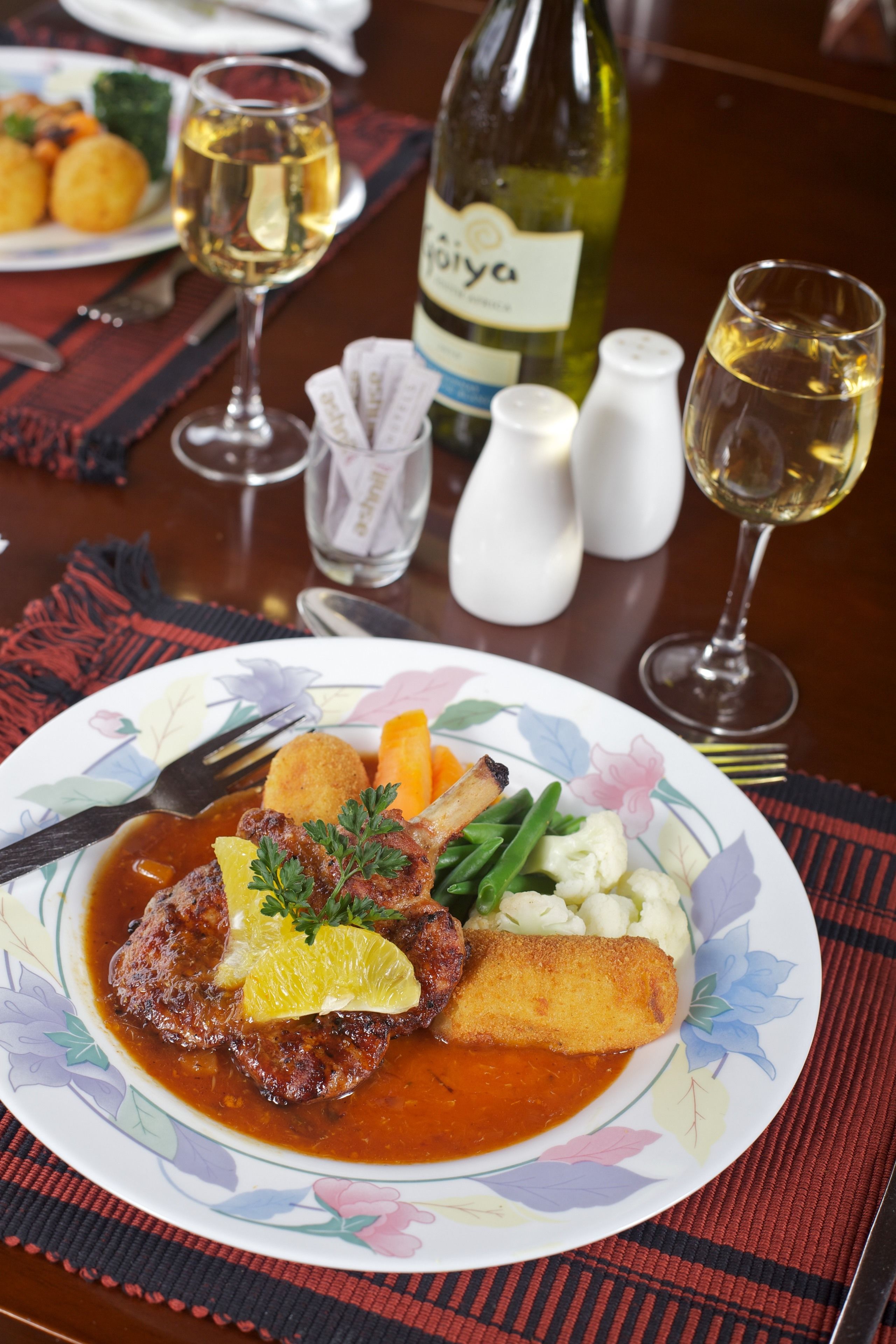 A dining table with a plate of food, a bottle of wine, and salt and pepper shakers.