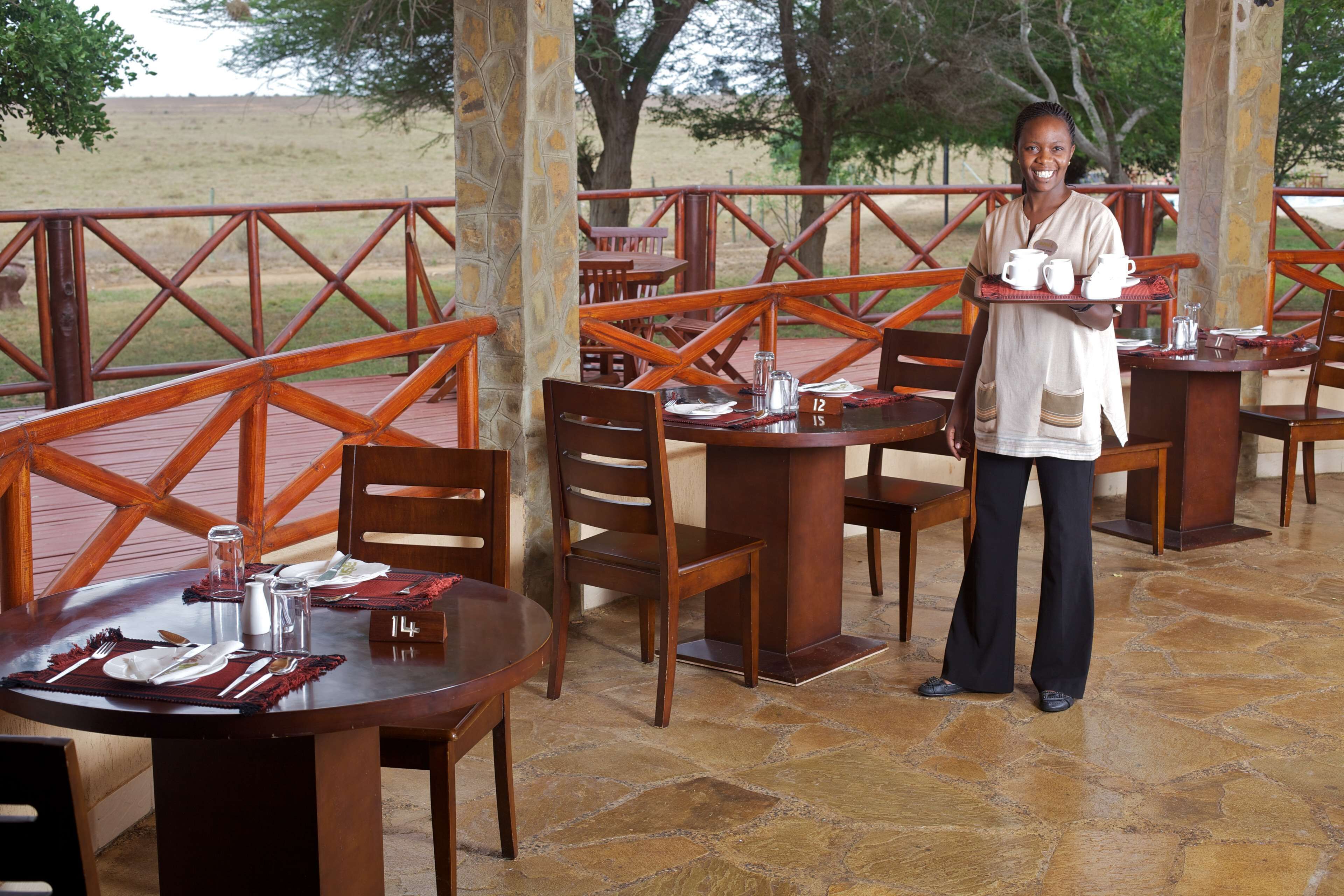 A restaurant with wooden tables and chairs, a stone floor, and a view of the outdoors.