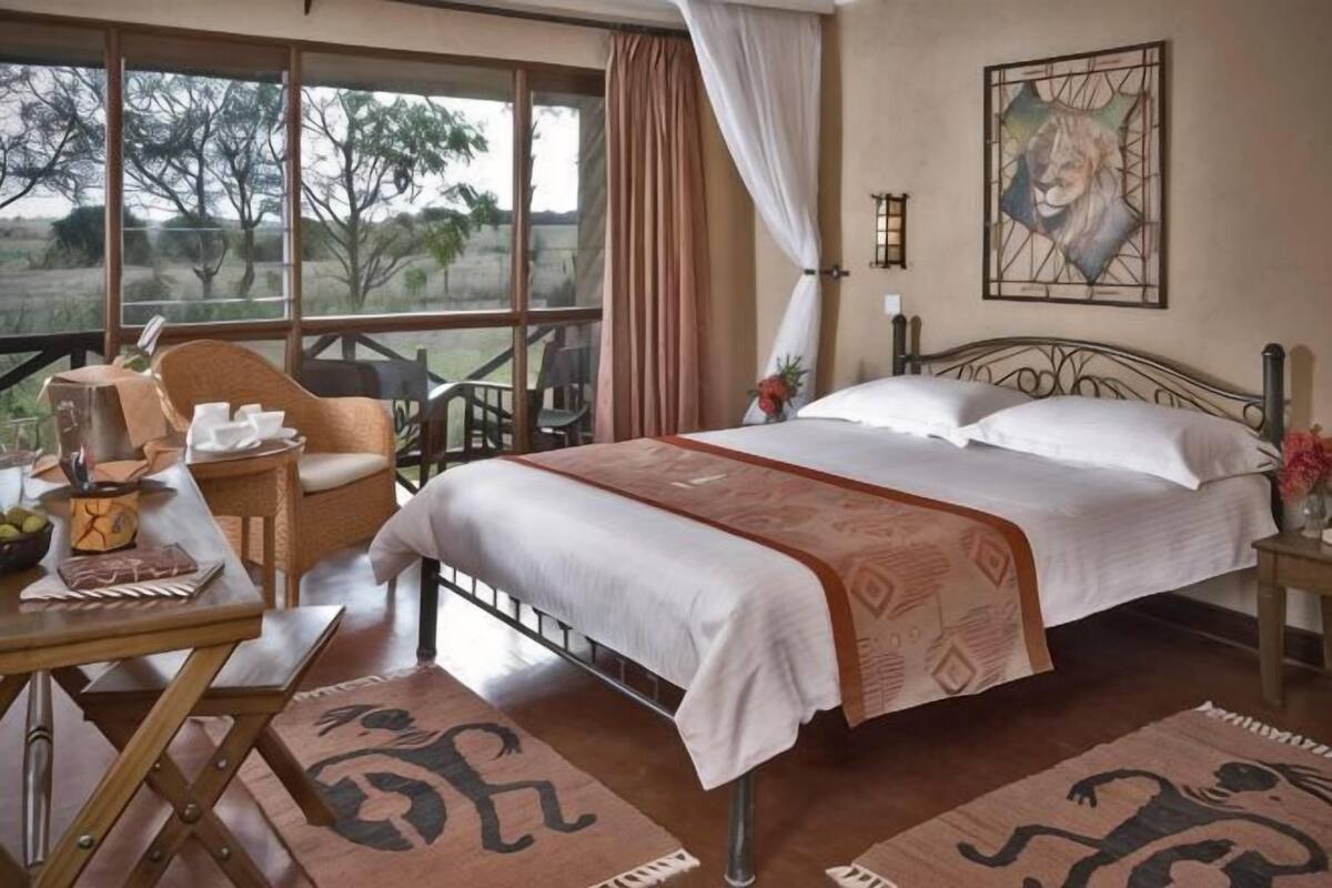 A bedroom with a large bed, a desk with a chair, a window with curtains, and a painting on the wall.