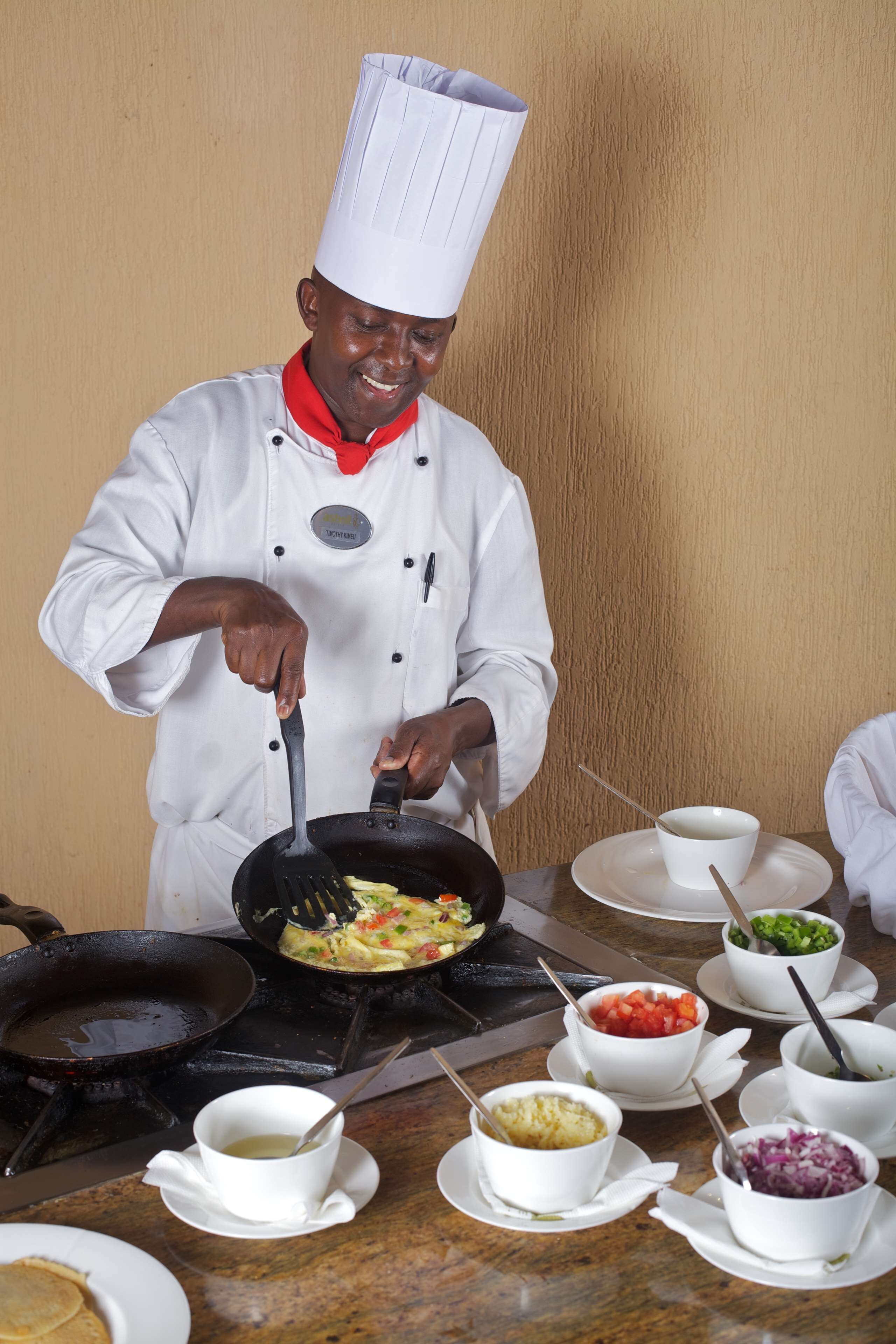 A chef cooking in a professional kitchen with various dishes and ingredients on the counter.