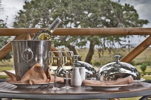 Une table dressée avec une bouteille de champagne, deux verres à vin, un pichet blanc, des salières et des poivrières, une serviette et un cloche en argent.
