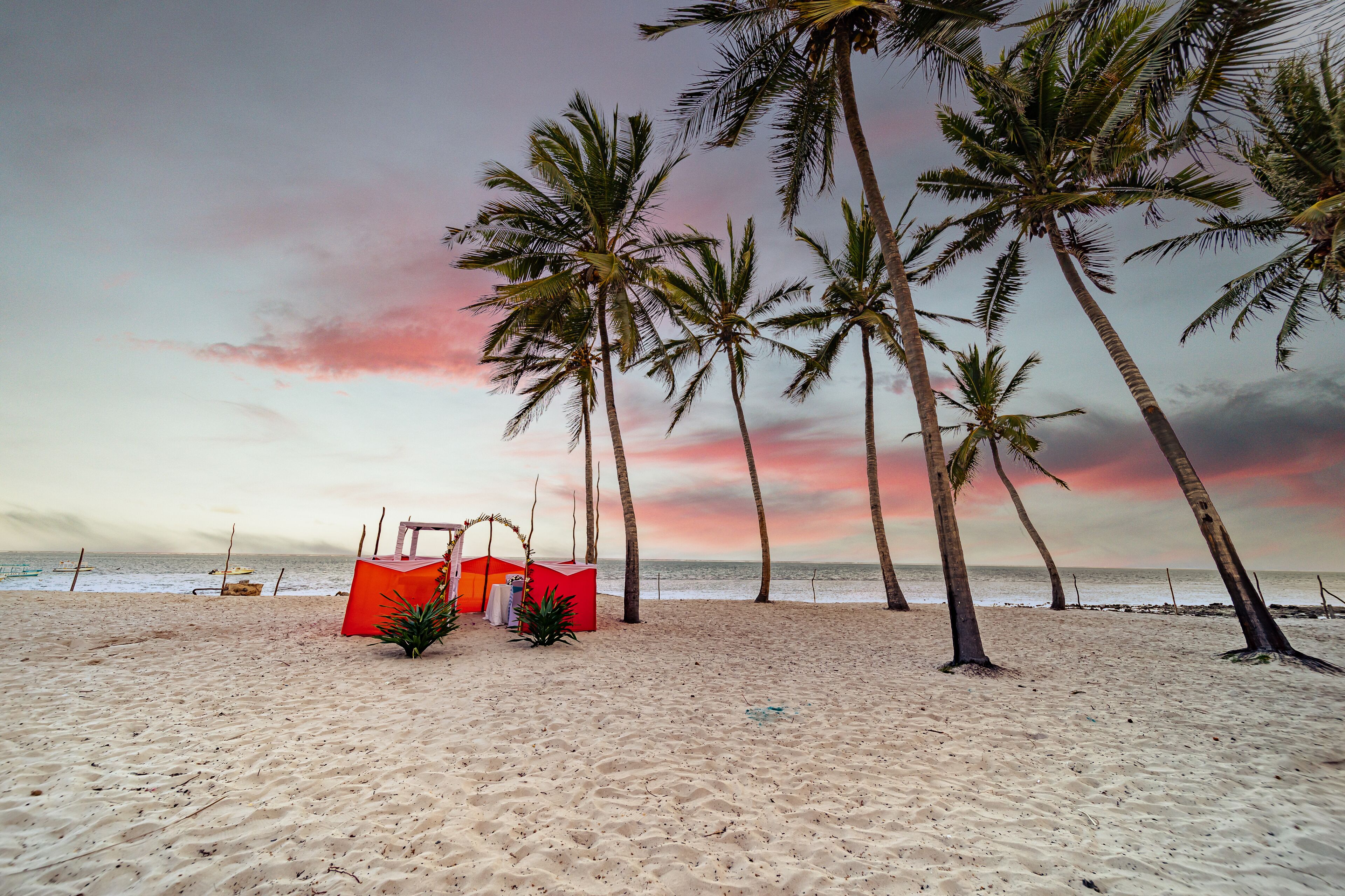 A beach with palm trees and a red structure, likely a beach hut or lounge.