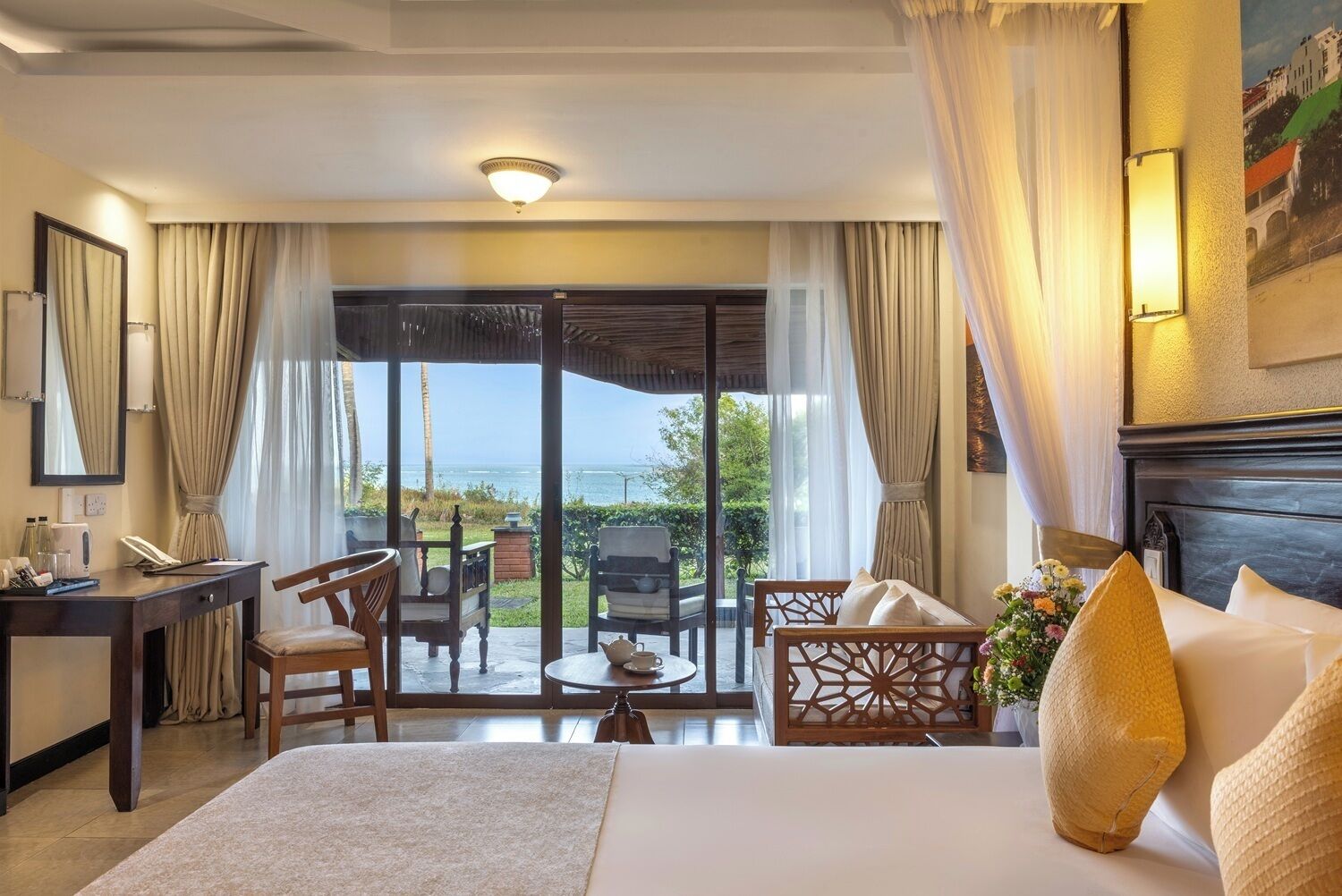 A hotel room with a bed, a desk, a chair, a table, and a view of the sea.