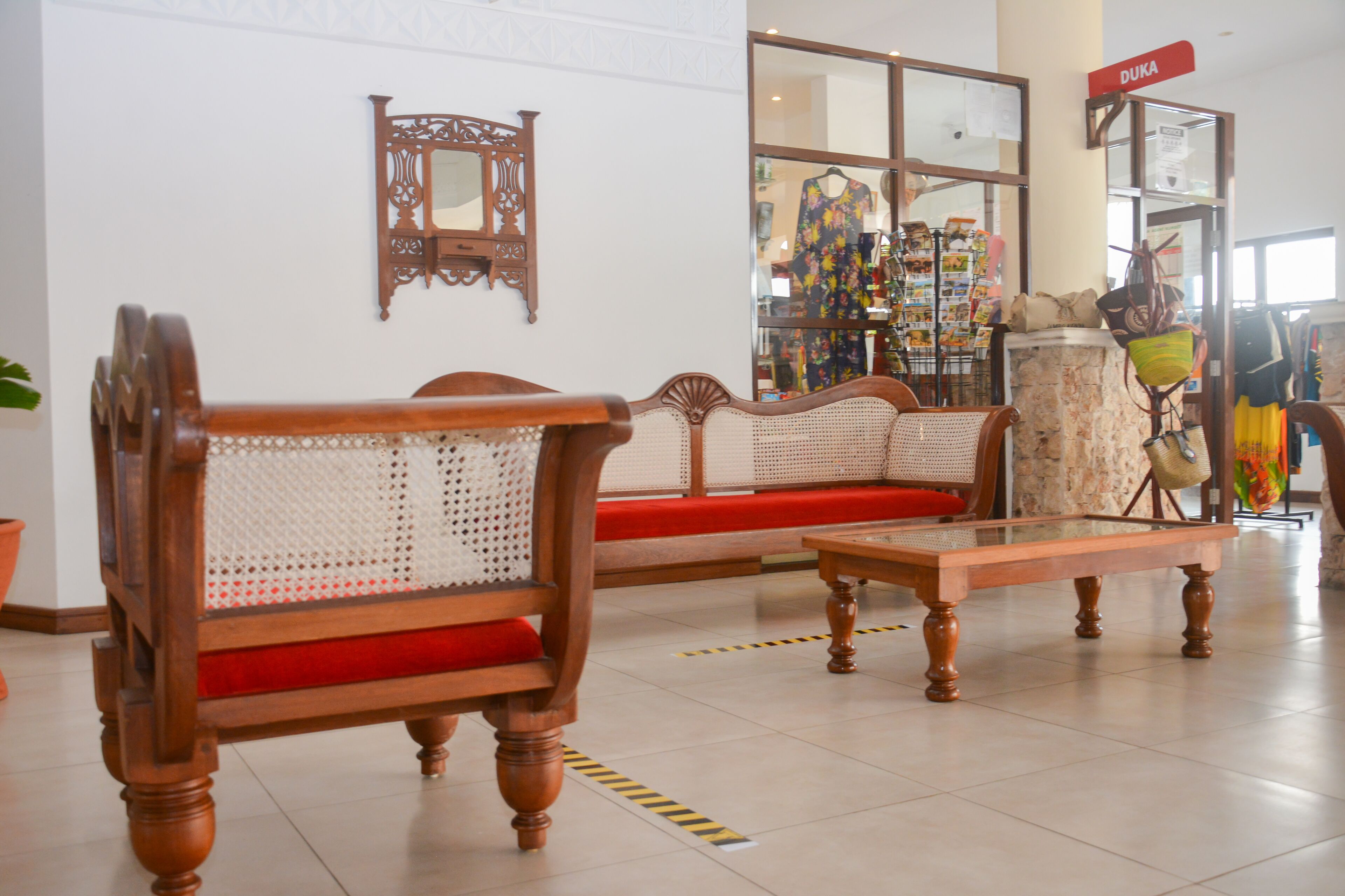 A lobby with a wooden sofa and a glass coffee table, a mirror, and a sign reading "DUKA".