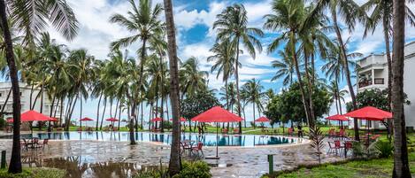 A pool area with red umbrellas and palm trees.