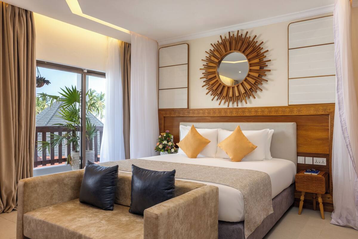 Habitación de hotel con una cama grande, un sofá, un espejo y vistas a palmeras.