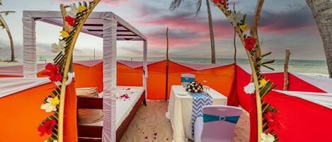 Una carpa de playa montada con toldo, camas y una mesa con un arreglo floral.