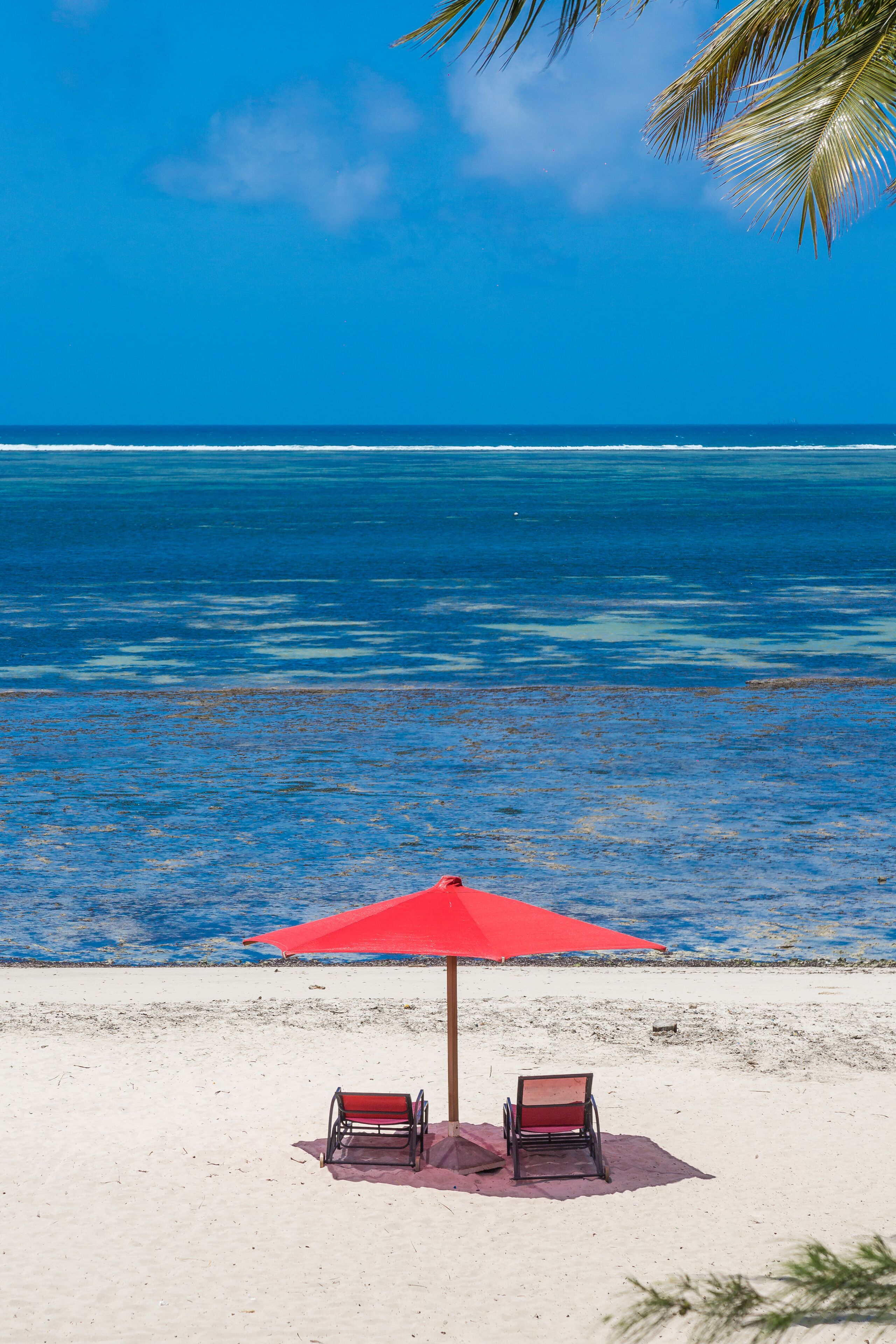 A beach with two red chairs under a red umbrella, facing the ocean.