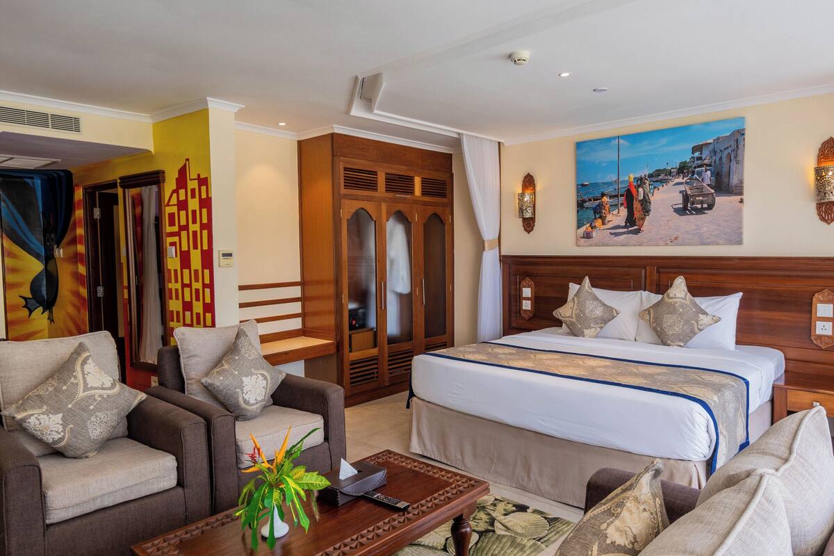 Habitación de hotel con cama, dos sillones, una mesa de centro y un cuadro en la pared.