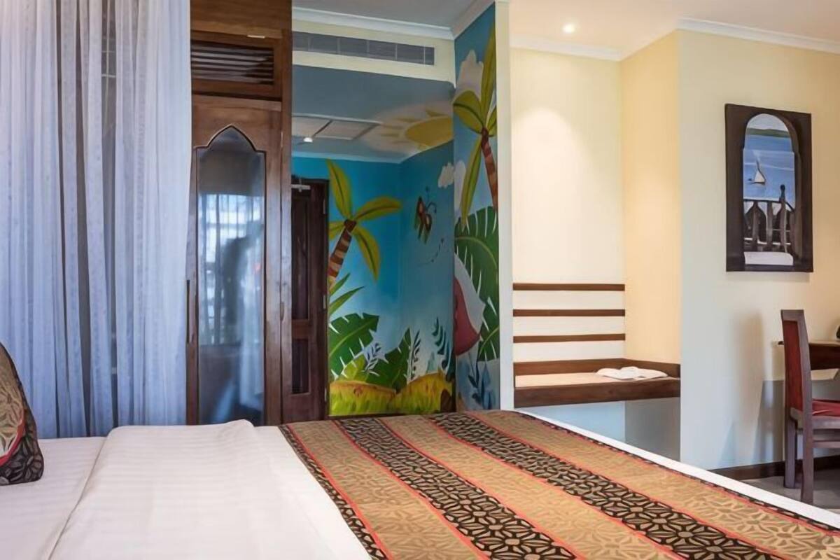 Una habitación de hotel con una cama, un mural, una ventana con cortinas y una pequeña mesa.