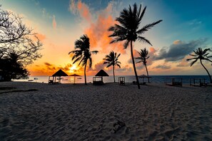 A beach with palm trees, beach huts, and the ocean at sunset. - PrideInn Paradise Beach Resort & Spa Mombasa (Mombasa)