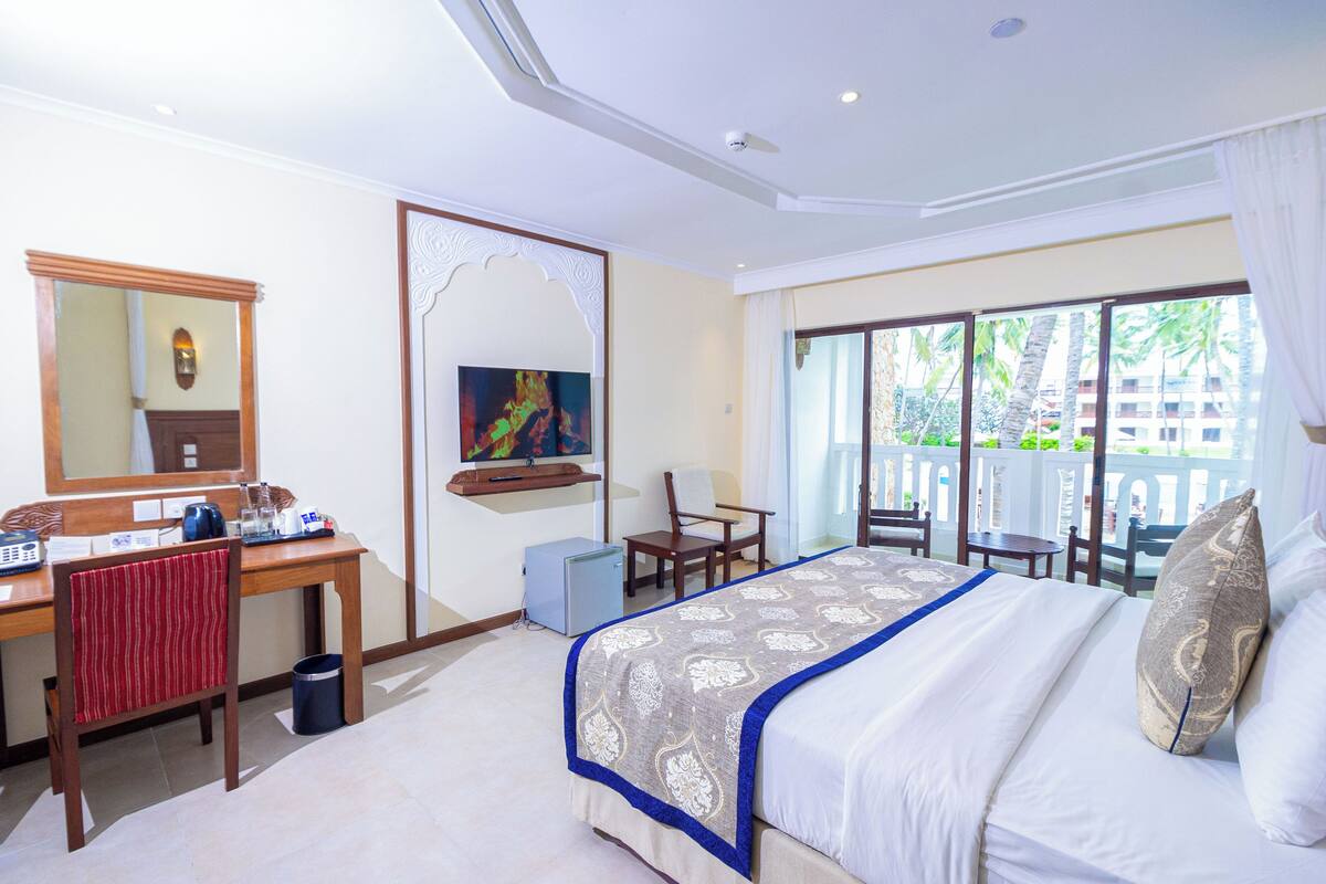 Habitación de hotel con cama, escritorio, silla y balcón con vistas.