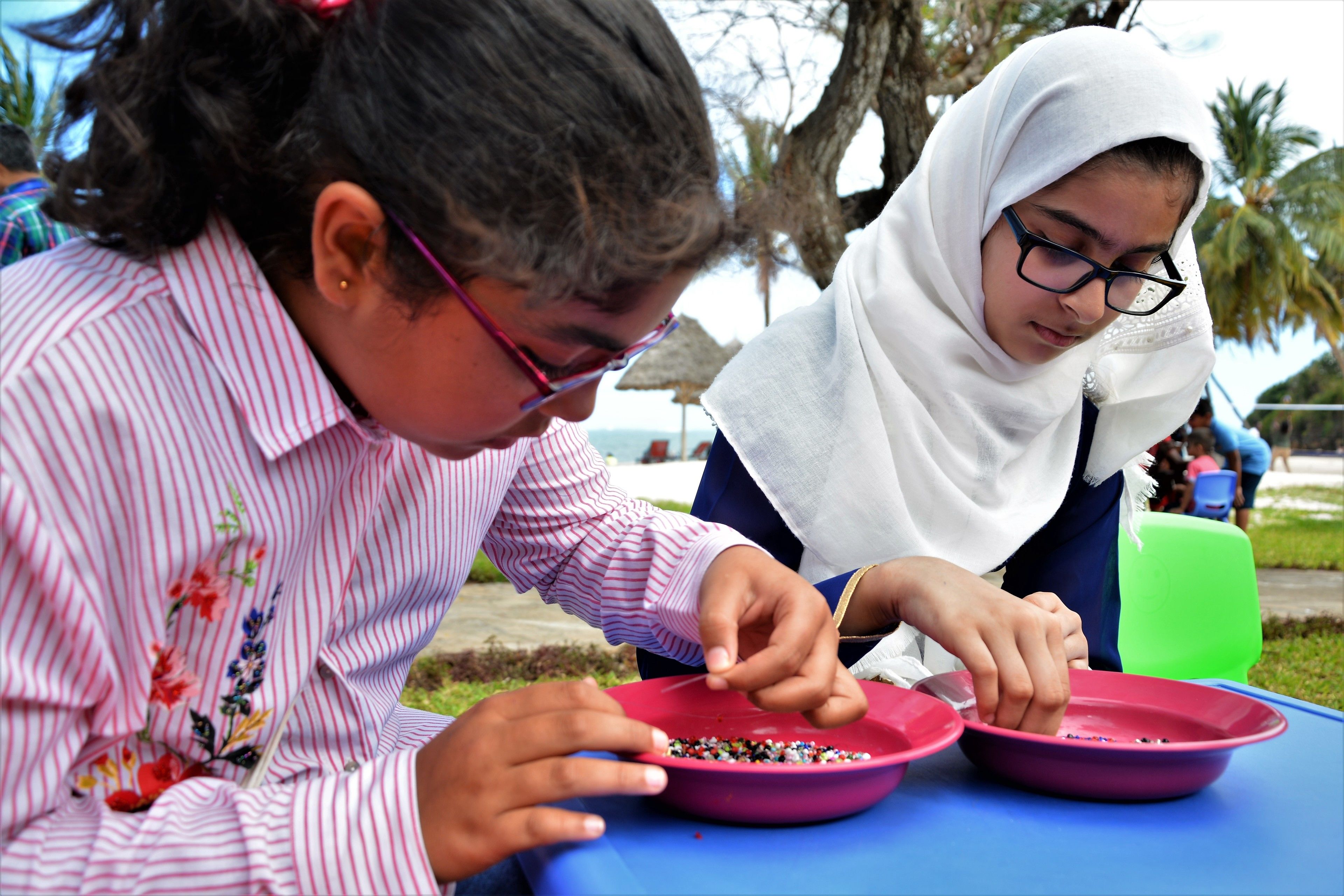 Two individuals seated at a table with pink bowls, engaged in an activity.