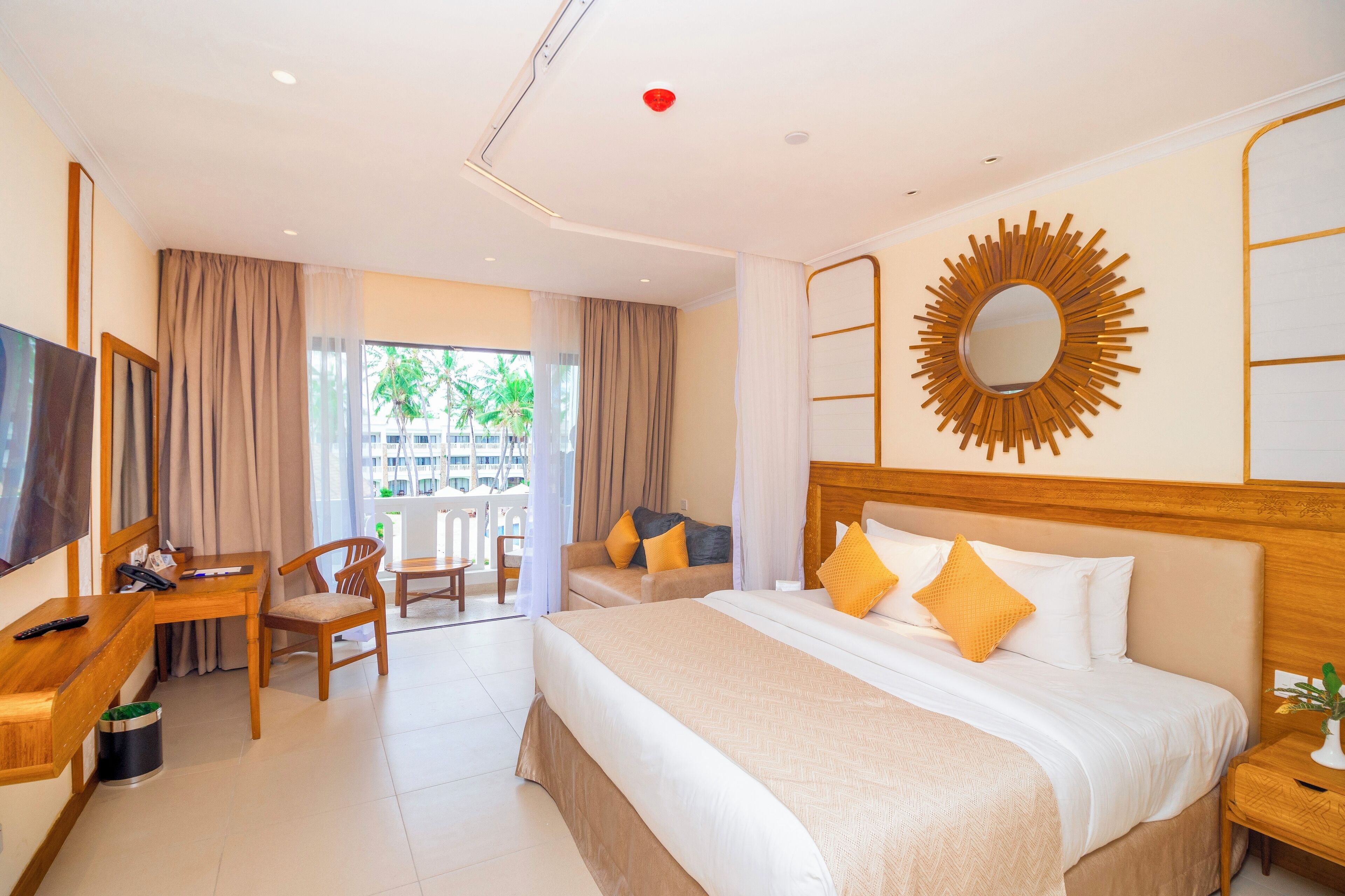 A hotel room with a large bed, a desk with a chair, a TV, and a balcony with curtains.
