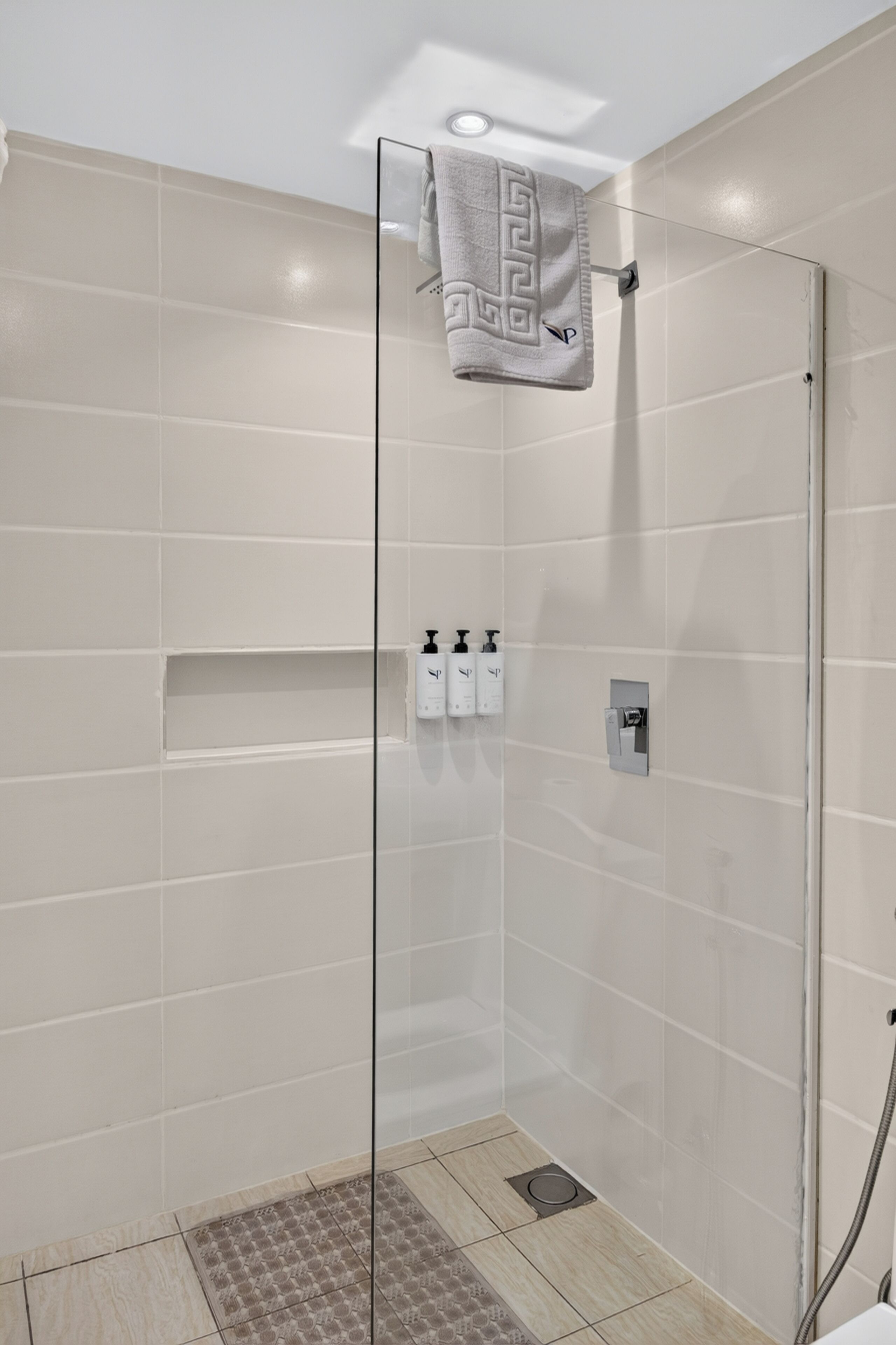 A glass-enclosed shower with beige tiles, a towel hanging on the wall, and a shower control panel.