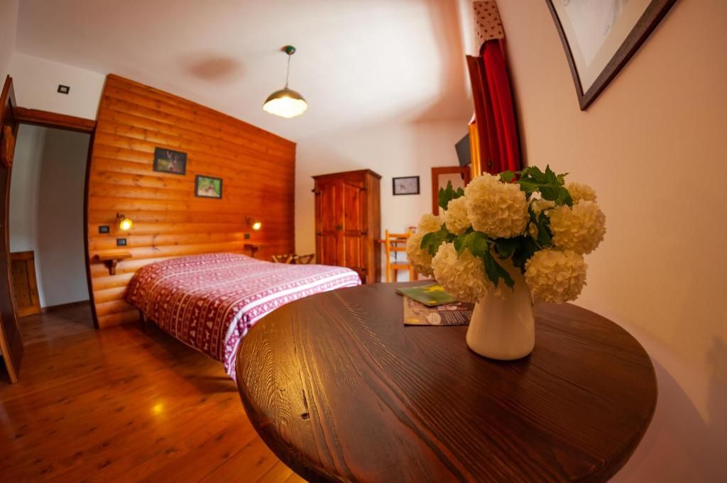 Una stanza accogliente con una parete in legno a tronchi, un tavolo rotondo in legno con un vaso di fiori e un letto con copriletto decorato.