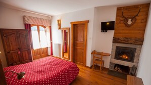 Un dormitorio con colcha roja, armario de madera, chimenea y televisor montado en la pared.