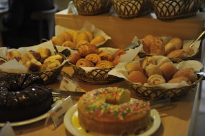 A variety of baked goods displayed in baskets and on plates, including pastries and a cake. - Bergson Flat (Caxias do Sul)