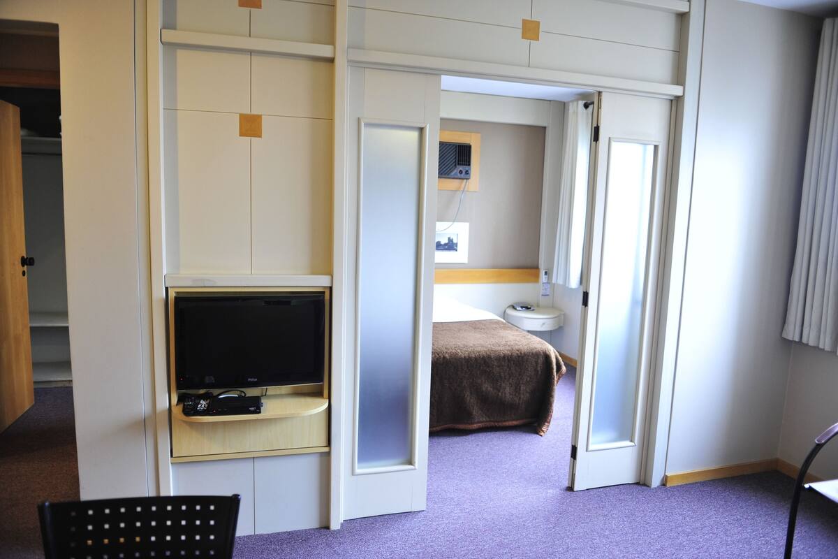 Une chambre d’hôtel équipée d’une télévision, d’un lit, d’une table de chevet et d’une chaise.