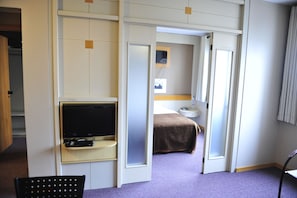 A hotel room with a television, a bed, a bedside table, and a chair. - Bergson Flat (Caxias do Sul)