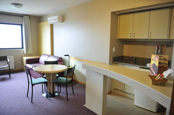 A compact kitchen with a dining area, featuring a round table, chairs, a sofa, and a small refrigerator.